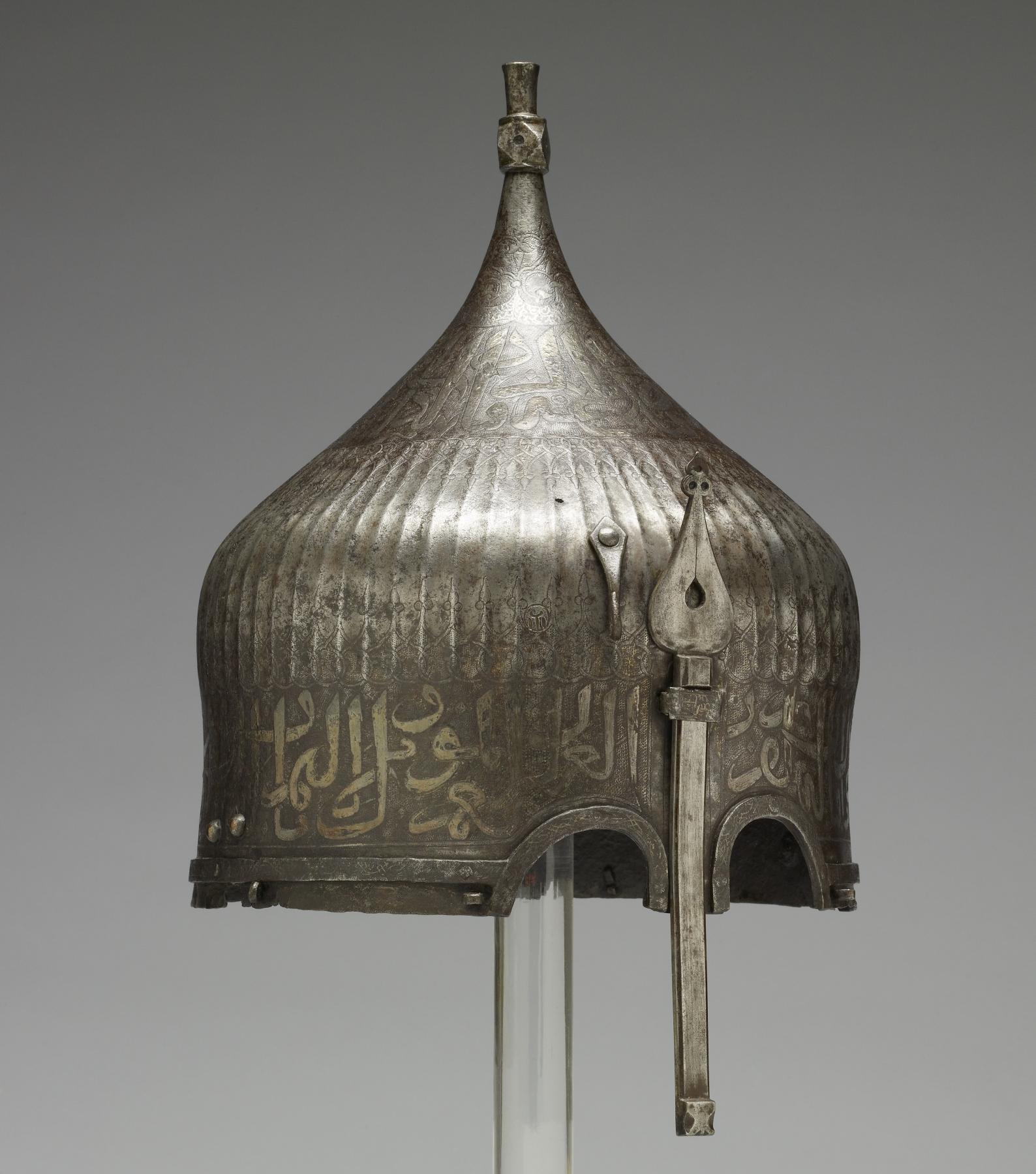 A warrior would have worn this helmet over a cloth turban. He would have been confident of being safeguarded in battle by the writing around the helmet's rim. The inscription from the Qur'an is garbled, however, indicating that its Iranian maker may not have known Arabic. Yet the presence of Arabic writing apparently was thought to be enough to invoke the protective power of God's word. This helmet once belonged to the St Irene royal arsenal in Istanbul Turkey as it bears the distinctive mark (tamga) composed of a circle enclosing a loop over three vertical lines, the stamp is clearly visible to the left of the nose guard on this helmet. It was probably part of the war booty amassed by the Ottoman Dynasty during the many wars between Turkey and Iran. Later, it was owned by the French painter Jean-Léon Gérôme, who traveled throughout the Near East and painted many scenes of Muslim life.