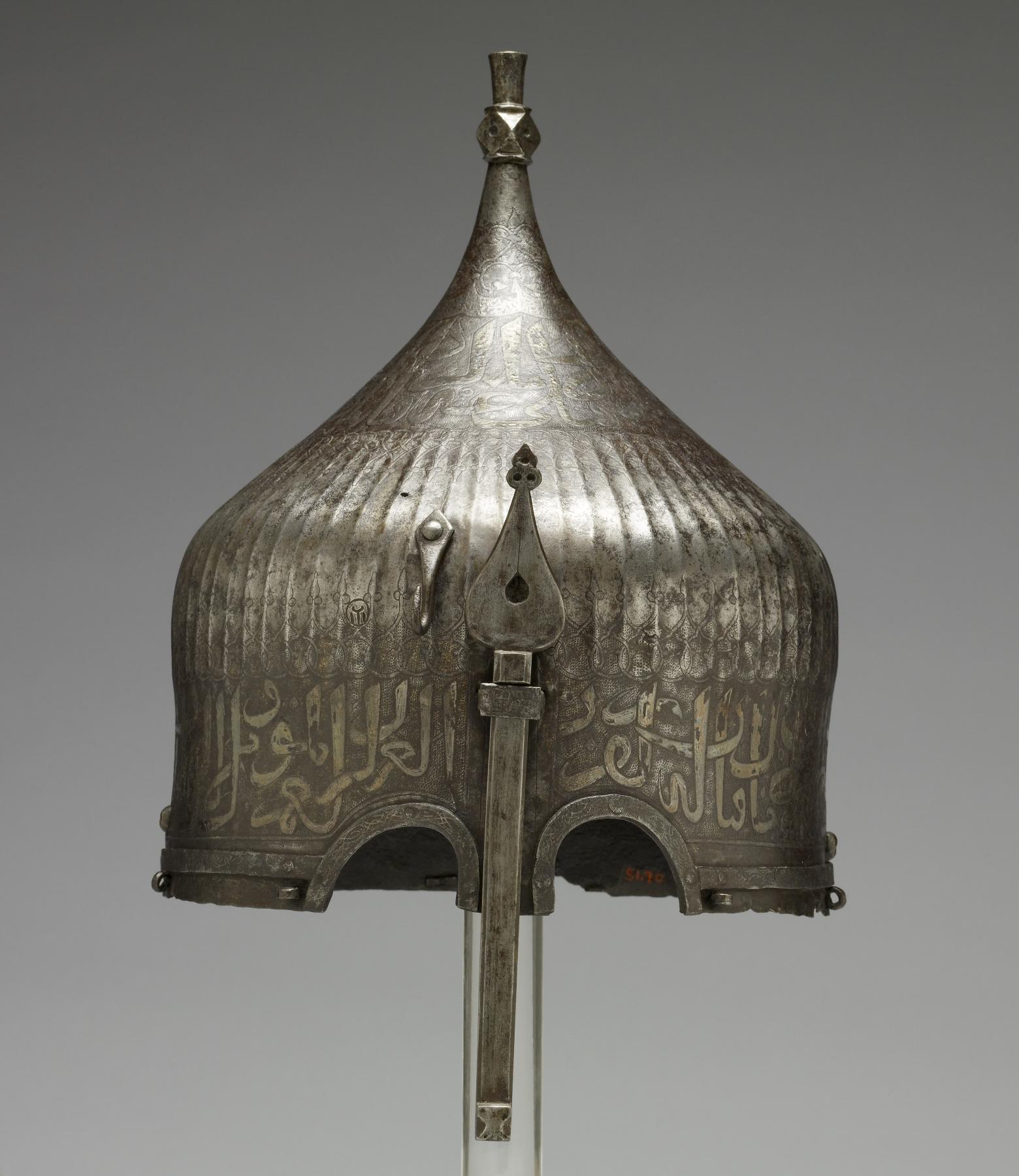 A warrior would have worn this helmet over a cloth turban. He would have been confident of being safeguarded in battle by the writing around the helmet's rim. The inscription from the Qur'an is garbled, however, indicating that its Iranian maker may not have known Arabic. Yet the presence of Arabic writing apparently was thought to be enough to invoke the protective power of God's word. This helmet once belonged to the St Irene royal arsenal in Istanbul Turkey as it bears the distinctive mark (tamga) composed of a circle enclosing a loop over three vertical lines, the stamp is clearly visible to the left of the nose guard on this helmet. It was probably part of the war booty amassed by the Ottoman Dynasty during the many wars between Turkey and Iran. Later, it was owned by the French painter Jean-Léon Gérôme, who traveled throughout the Near East and painted many scenes of Muslim life.