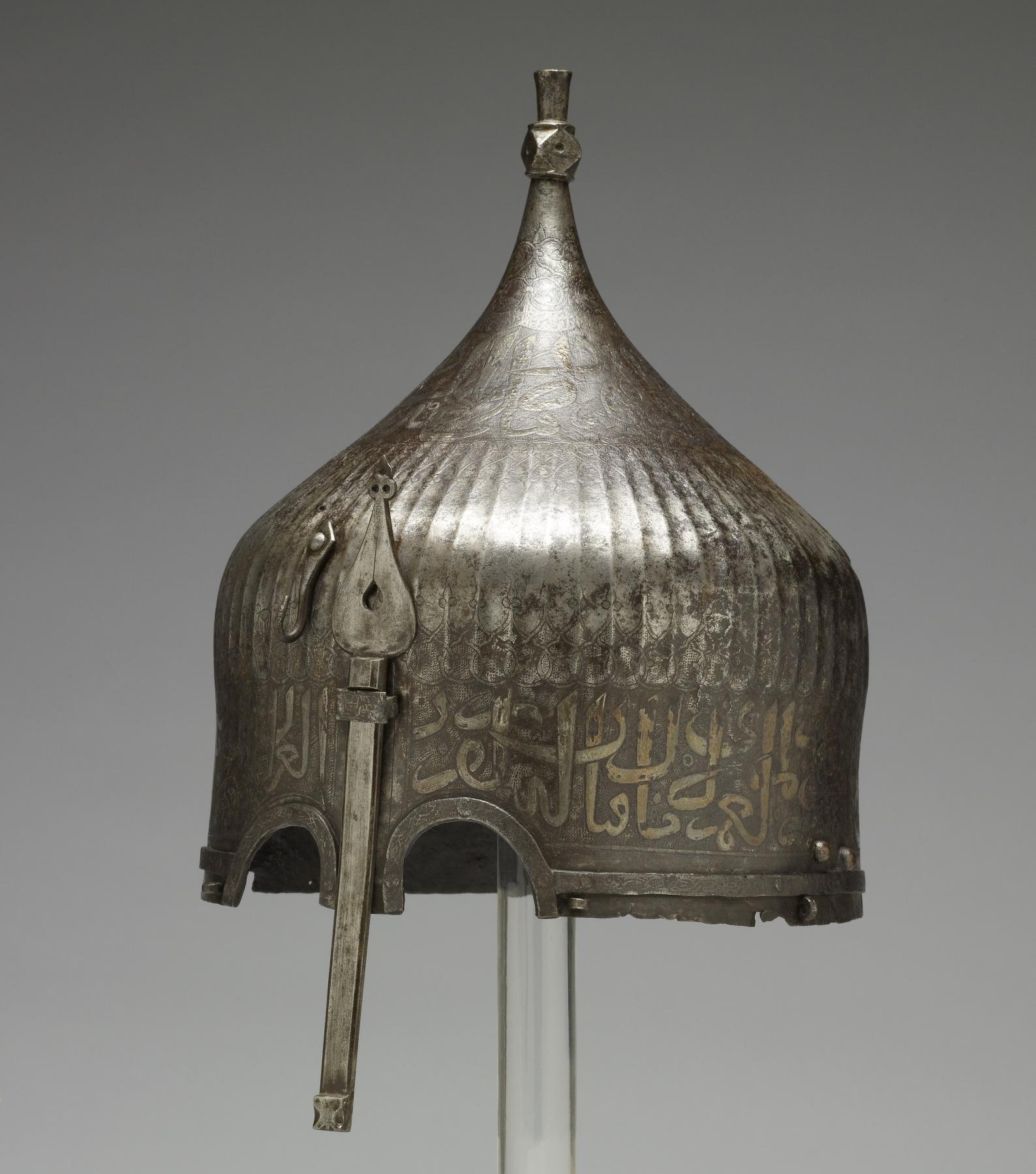 A warrior would have worn this helmet over a cloth turban. He would have been confident of being safeguarded in battle by the writing around the helmet's rim. The inscription from the Qur'an is garbled, however, indicating that its Iranian maker may not have known Arabic. Yet the presence of Arabic writing apparently was thought to be enough to invoke the protective power of God's word. This helmet once belonged to the St Irene royal arsenal in Istanbul Turkey as it bears the distinctive mark (tamga) composed of a circle enclosing a loop over three vertical lines, the stamp is clearly visible to the left of the nose guard on this helmet. It was probably part of the war booty amassed by the Ottoman Dynasty during the many wars between Turkey and Iran. Later, it was owned by the French painter Jean-Léon Gérôme, who traveled throughout the Near East and painted many scenes of Muslim life.