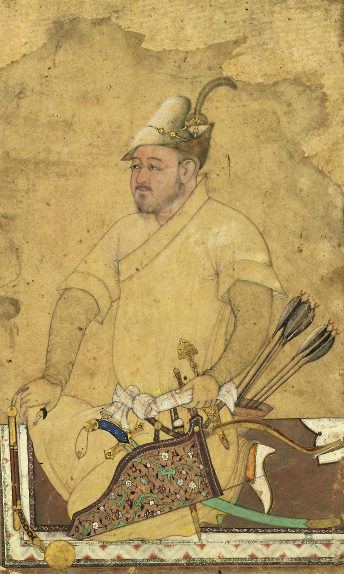 Gouache heightened with gold on paper, the heavily armed warrior with a very finely painted face kneels upon a medallion carpet wearing a robe with short sleeves and an adorned fur hat, a mace, daggers, bow and arrow and shamshir amongst his weapons 17.3 x 10.5cm.